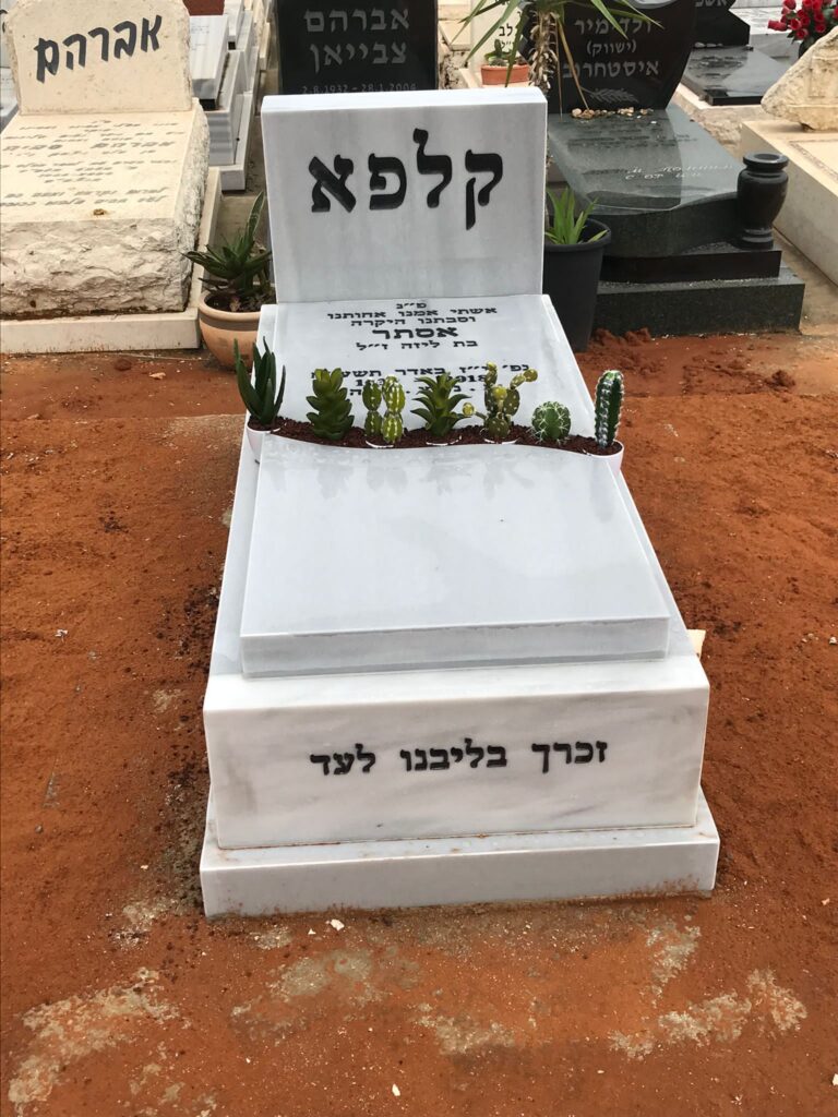 מצבה לבנה משיש עם חריטה בעברית וסוקולנטים על משטח הקבר