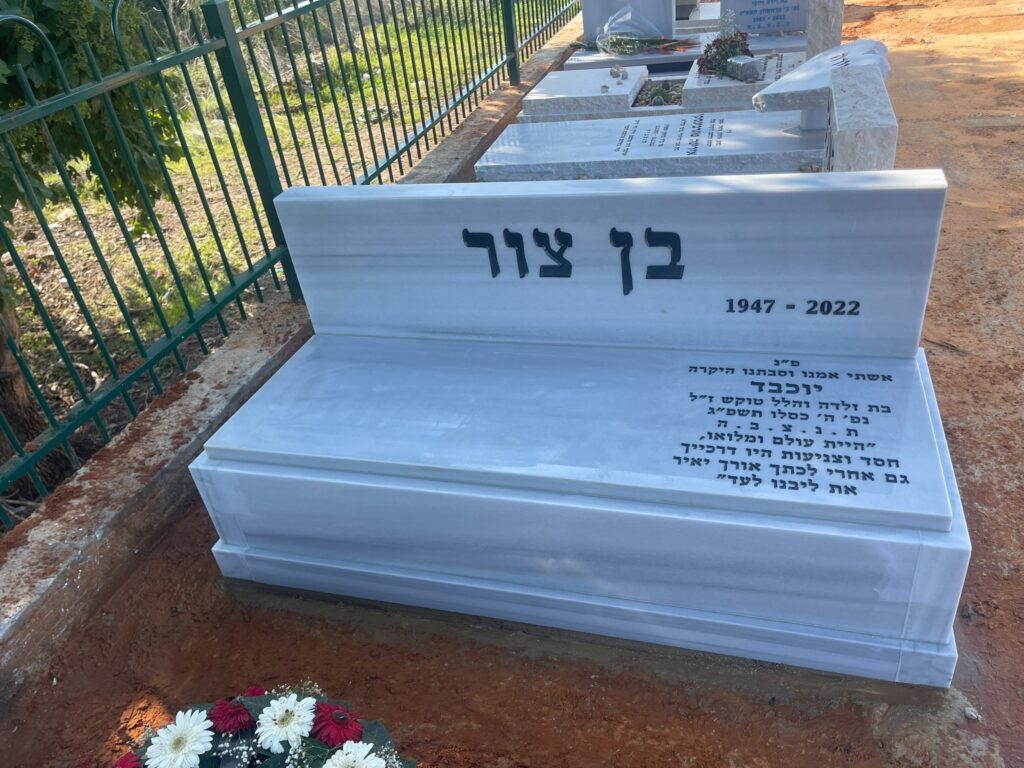 מצבה לבנה מעוצבת בבית עלמין עם כיתוב בעברית ותאריך