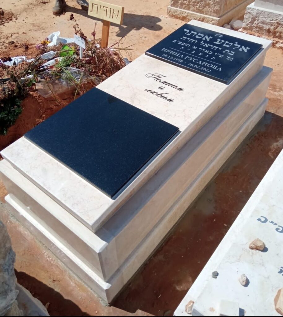 מצבה לבנה מעוצבת עם לוחות שיש שחורים וחריטה בבית העלמין.