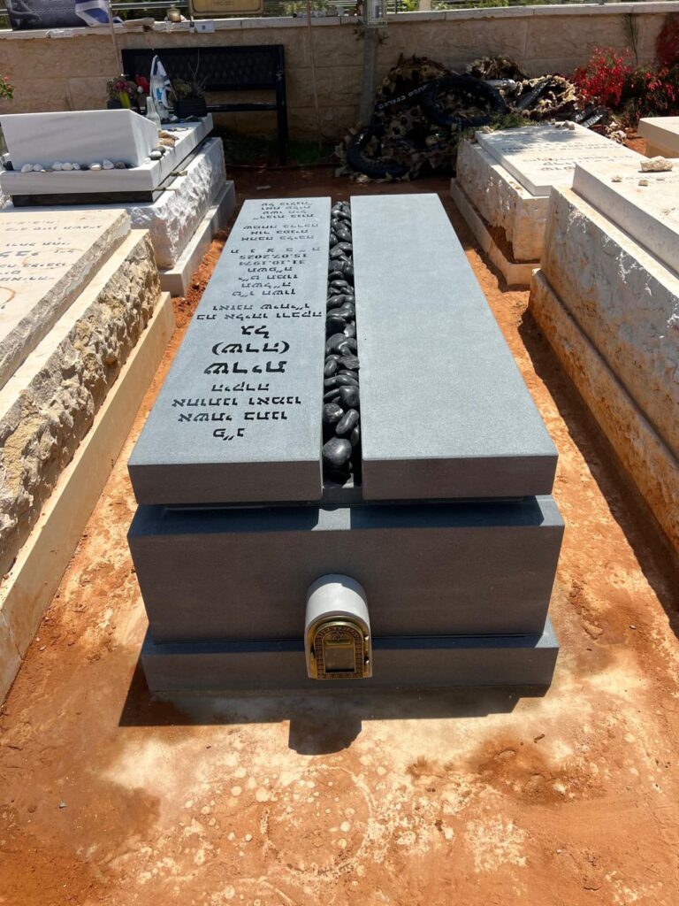 מצבה מודרנית מאבן אפורה עם חריטה בעברית ומילוי אבנים בבית עלמין
