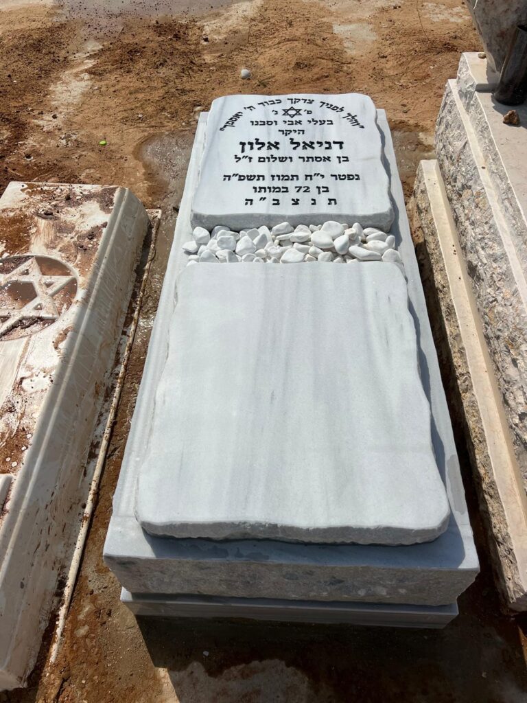 מצבת שיש לבנה עם כיתוב עברי ואבני זיכרון בבית עלמין